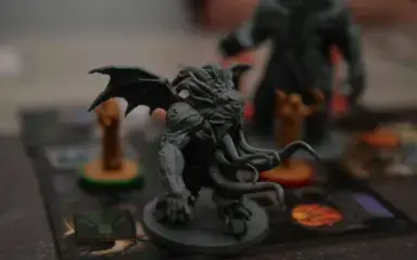 A detailed miniature figurine of a winged, tentacled creature is positioned on a game board. It conveys a menacing, fantastical atmosphere with muted colors.