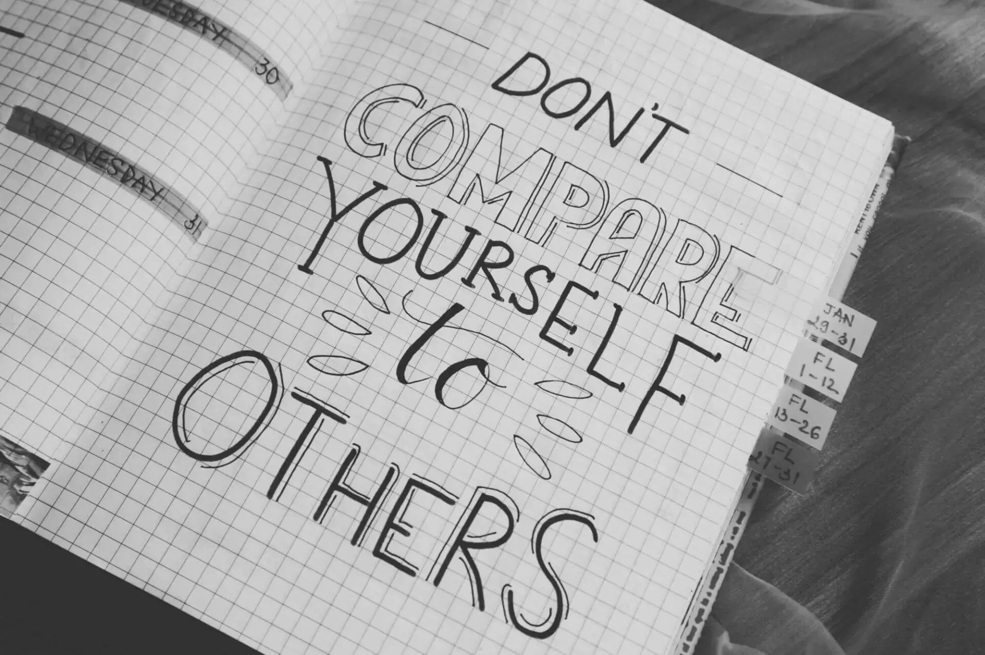 A handwritten motivational quote in a notebook reads, "Don't compare yourself to others," on graph paper. Tabs are visible, adding an organized tone.